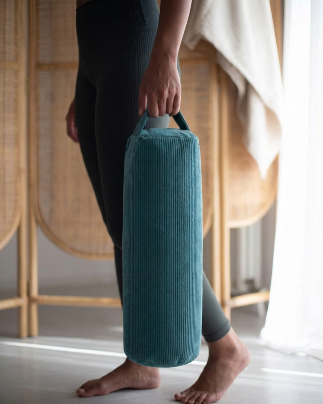 Professeure de yoga transportant un bolster bleu vert Awena Studio par sa poignée