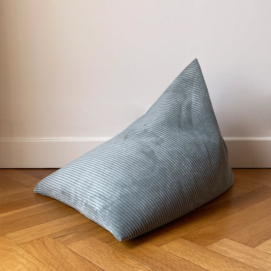 Coussin de méditation type Berlingot Awena Studio bleu vert en velours côtelé posé sur du parquet devant un mur blanc.