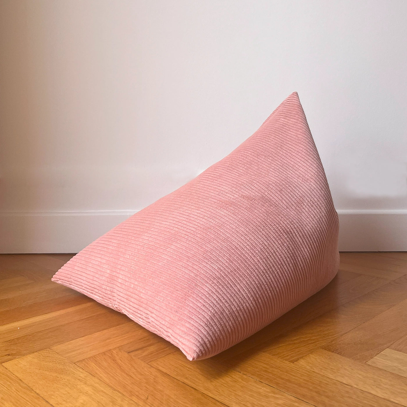 Coussin de méditation type Berlingot Awena Studio rose poudré en velours côtelé posé sur du parquet devant un mur blanc.