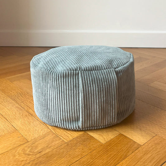 Coussin de méditation type Zafu Awena Studio bleu vert en velours côtelé posé sur du parquet devant un mur blanc.