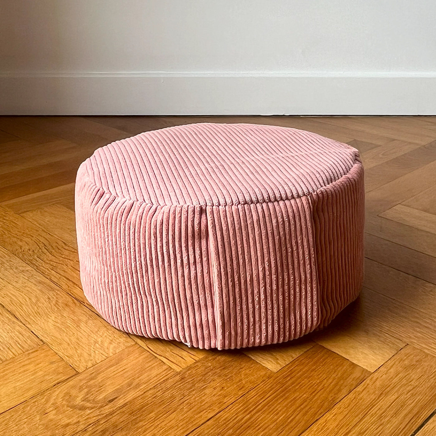 Coussin de méditation type Zafu Awena Studio rose poudré en velours côtelé posé sur du parquet devant un mur blanc.