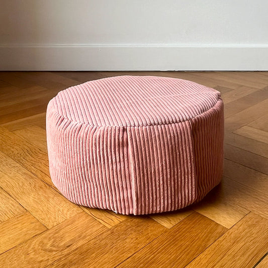 Coussin de méditation type Zafu Awena Studio rose poudré en velours côtelé posé sur du parquet devant un mur blanc.